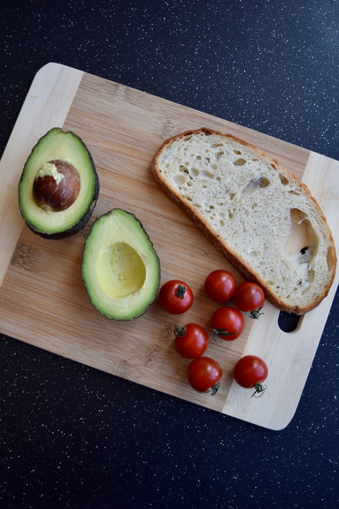 sourdough toast, avocado and tomatoes on a wooden cutting board