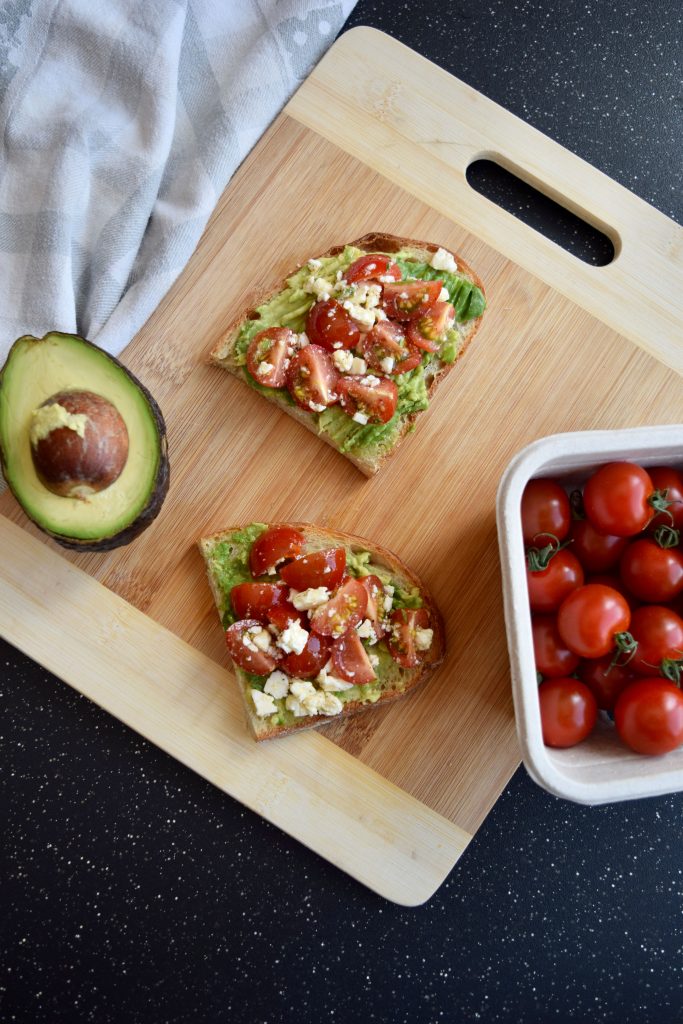 Toast, avocado and tomatoes on a wooden cutting board