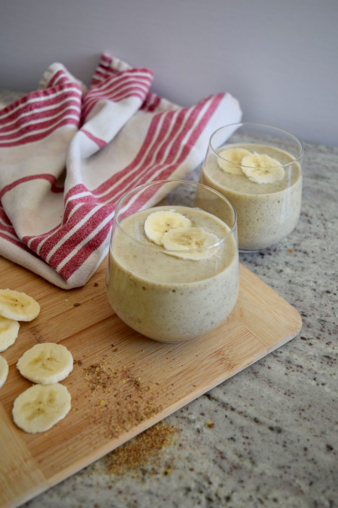 two pineapple smoothies on a wooden cutting board, banana slices to the side and a napkin in the distance