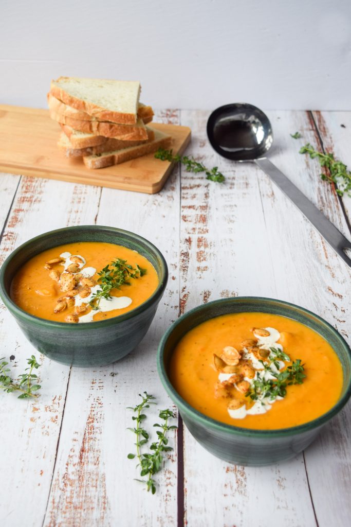 2 green bowls filled with butternut squash soup, topped with cream, squash seeds and fresh thyme.