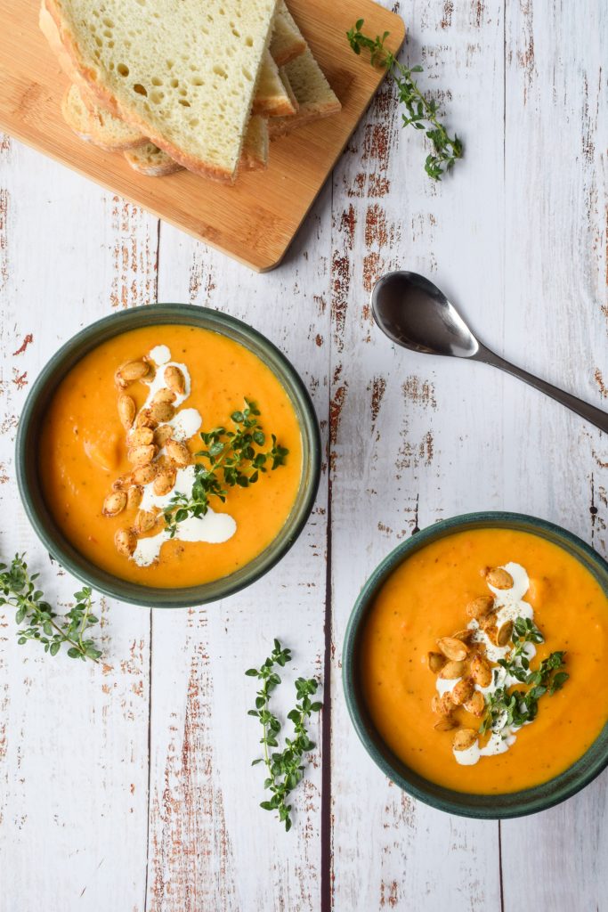 2 bowls of butternut squash soup in green bowls, topped with cream, roasted seeds and herbs.
