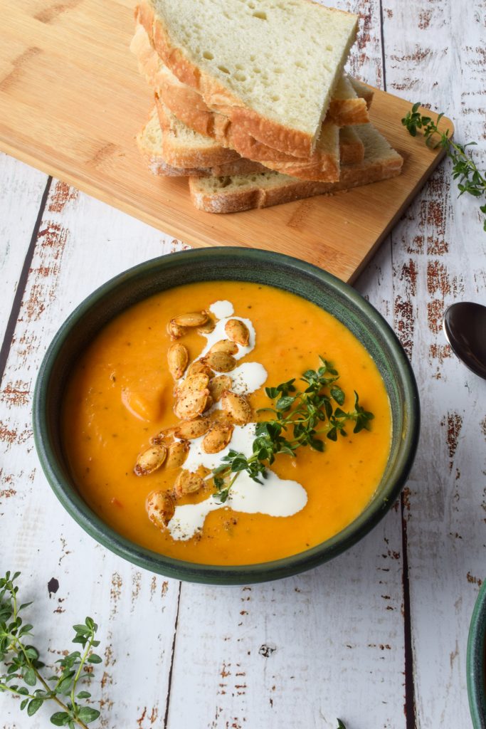 close up shot of an orange vegetable soup in a green bowl.