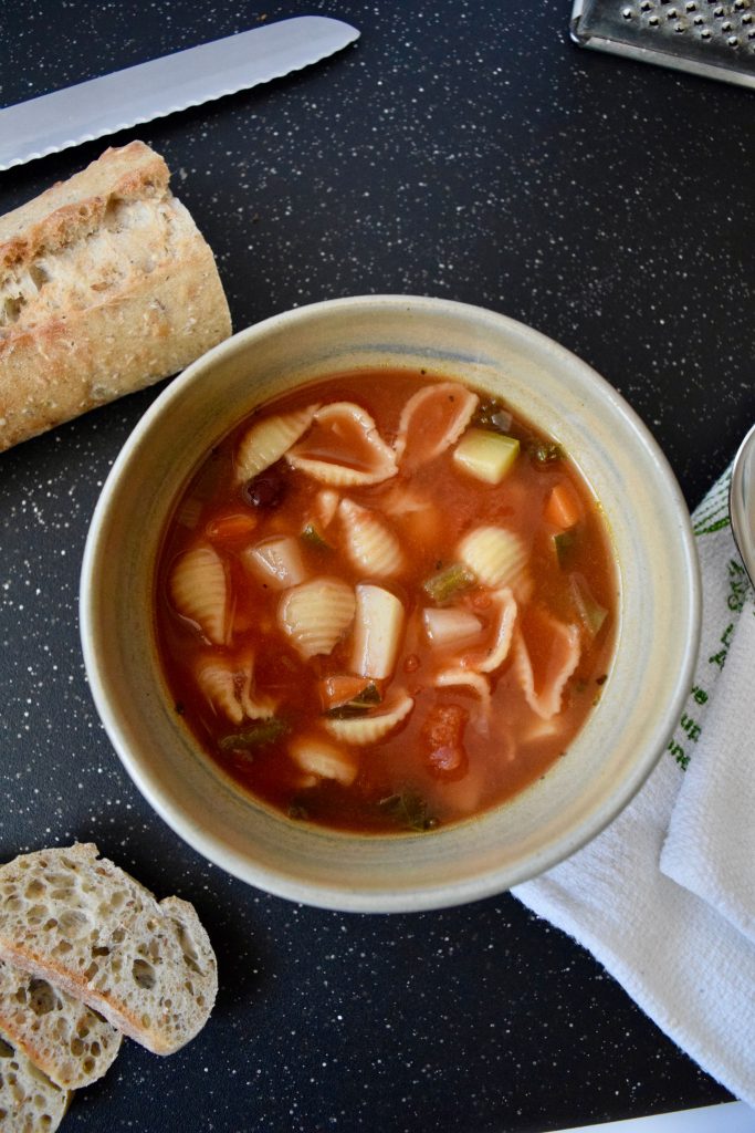 minestrone soup in a beige bowl, baguette slices on side