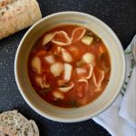 minestrone soup in a beige bowl, baguette slices on side