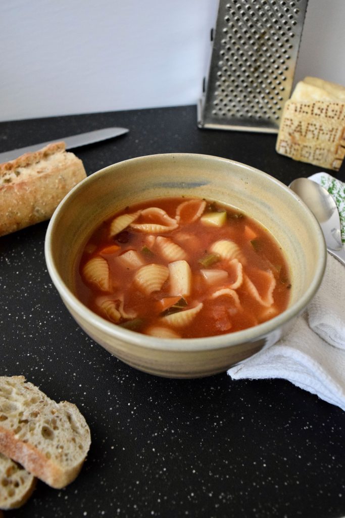 minestrone soup in a beige bowl, baguette slices on side