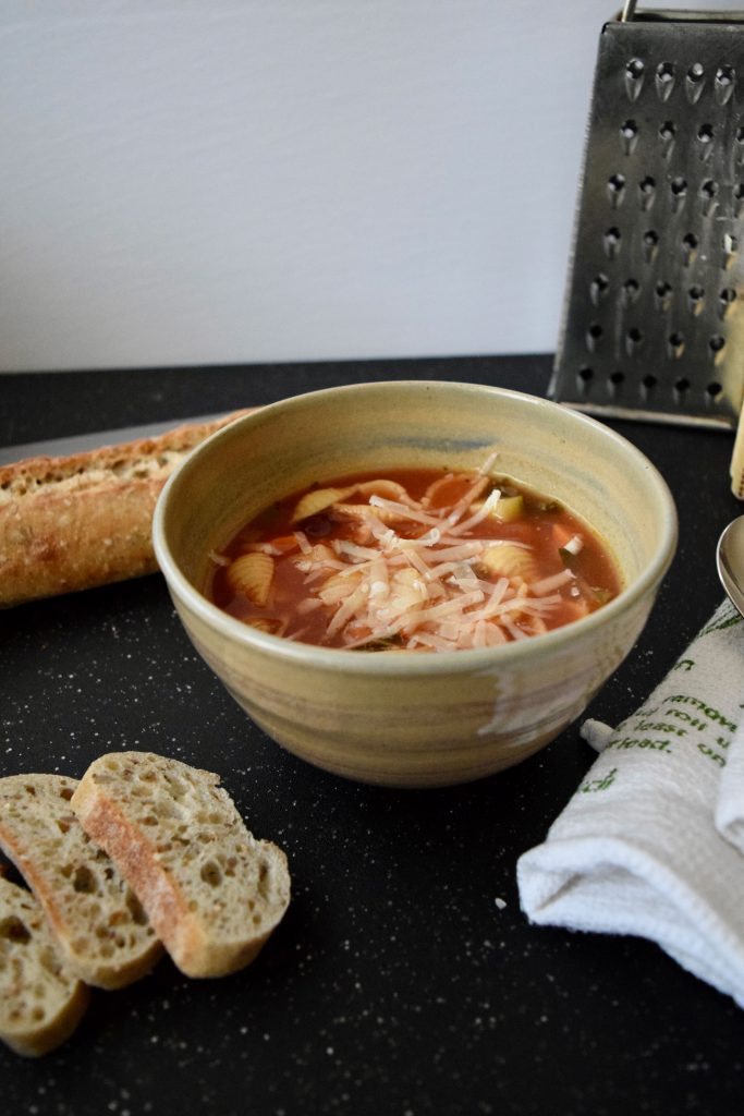 soup topped with parmesan cheese, grater and baguette in distance