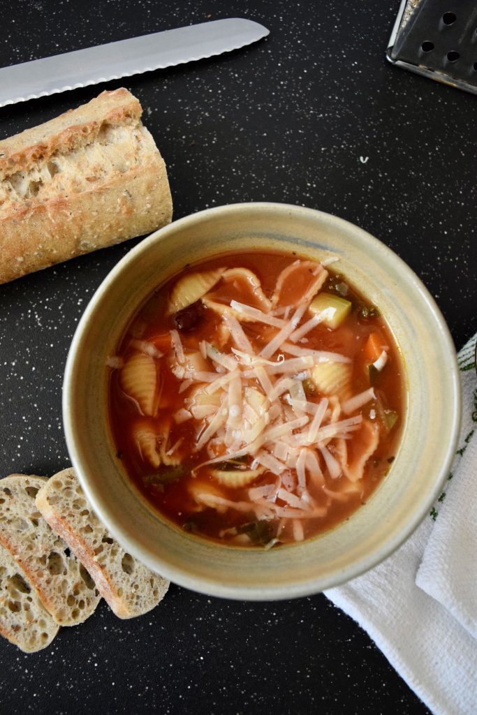 Soup in beige bowl, topped with parmesan cheese, baguette sliced on the side