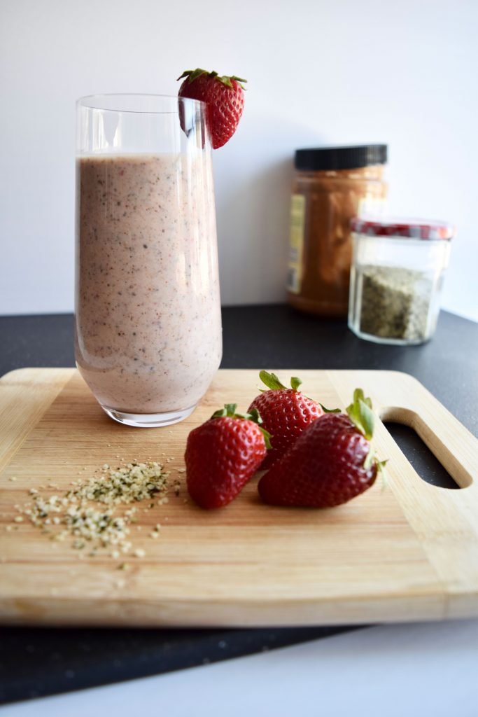 smoothie on a wooden cutting board, 2 strawberries and hemp seeds in the background, 2 jars in the background