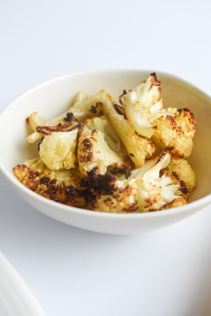 small white bowl filled with roasted cauliflower on a white backdrop