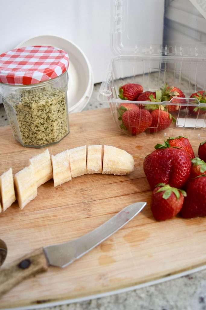 Chopped banana and strawberries on a wooden cutting board with a knife