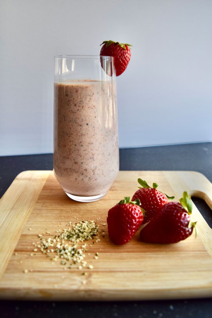 smoothie on a wooden cutting board, 2 strawberries and hemp seeds in the background