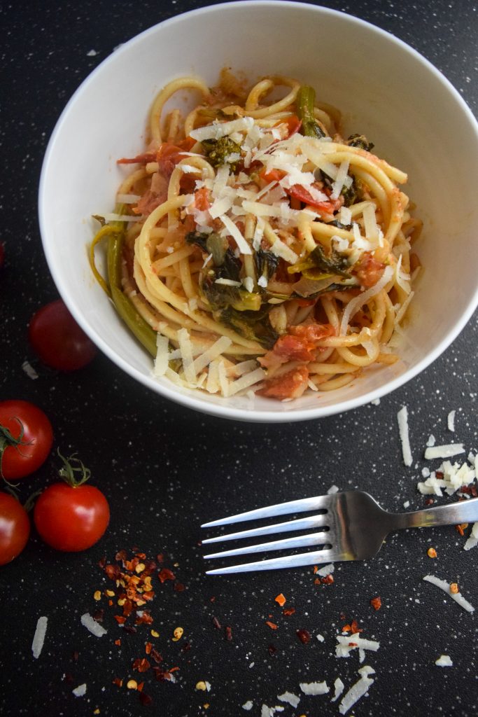 tomato and rapini pasta topped with cheese in a white bowl, on a black speckled tabletop