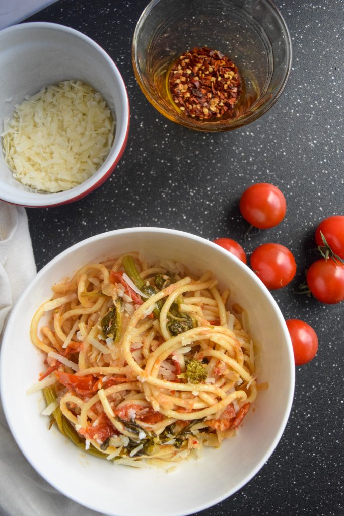 spaghetti topped with cheese in a white bowl, surrounded by smaller bowls, tomatoes and a fork