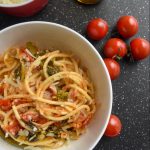 tomato and rapini pasta topped with cheese in a white bowl, surrounded by smaller bowls, tomatoes and a fork