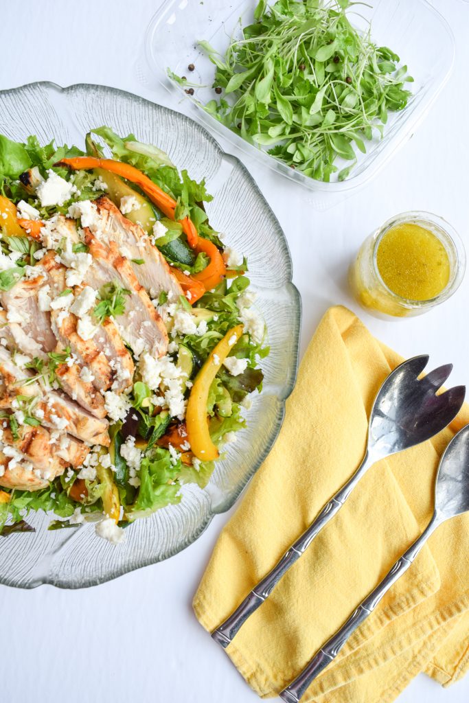 Glass salad bowl filled with chicken fajita-inspired salad. Yellow cloth napkin with utensils to the right, glass jar and 