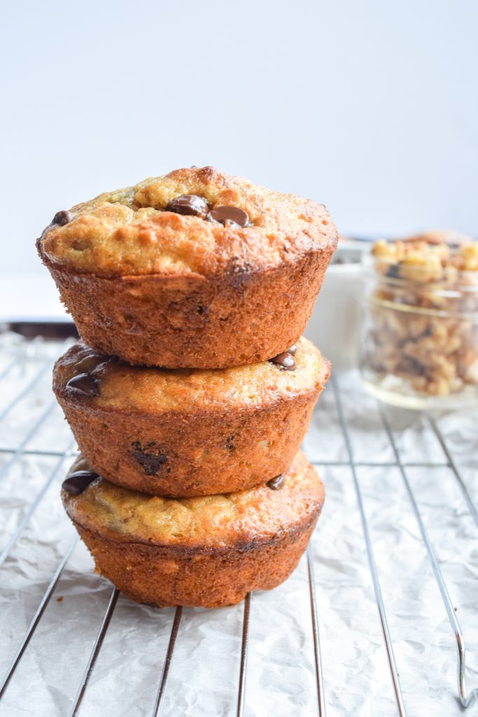 3 muffins stacked on top of each other, on top of a cooling rack and parchment paper. Jar filled with walnuts off in the distant