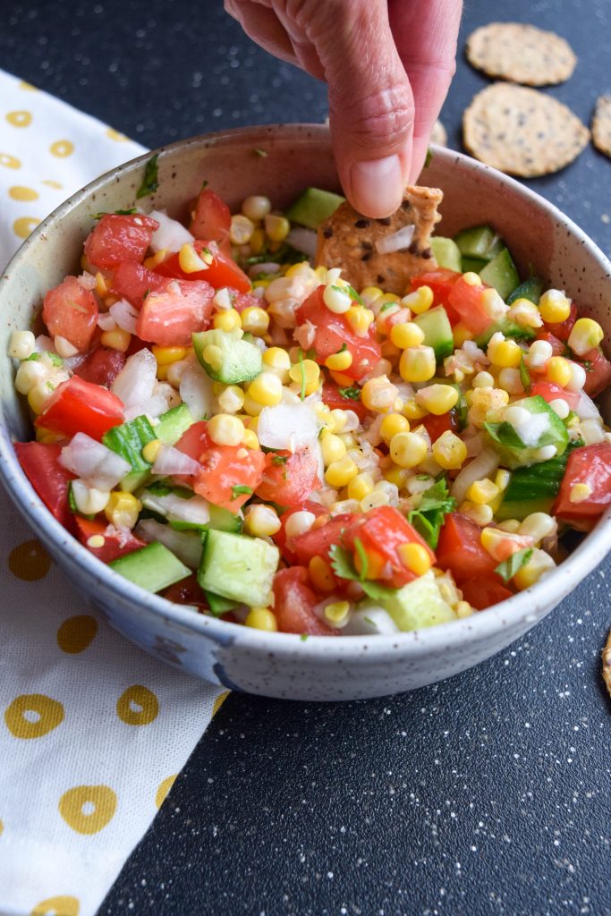 close up shot of corn salsa with a hand dipping inside
