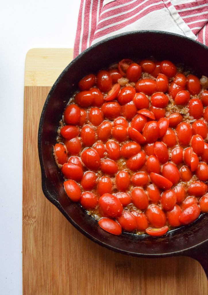 cast-iron skillet filled with cherry tomatoes cooked in oil