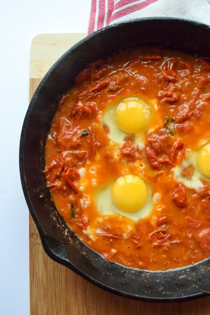 3 eggs poaching in a tomato sauce for shakshuka in a cast-iron skillet