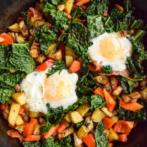 Two poached eggs cooked with red peppers, kale, bacon and potatoes.
