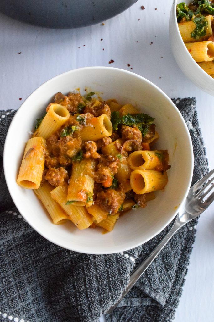 White bowl with squash and sausage pasta on a grey towel