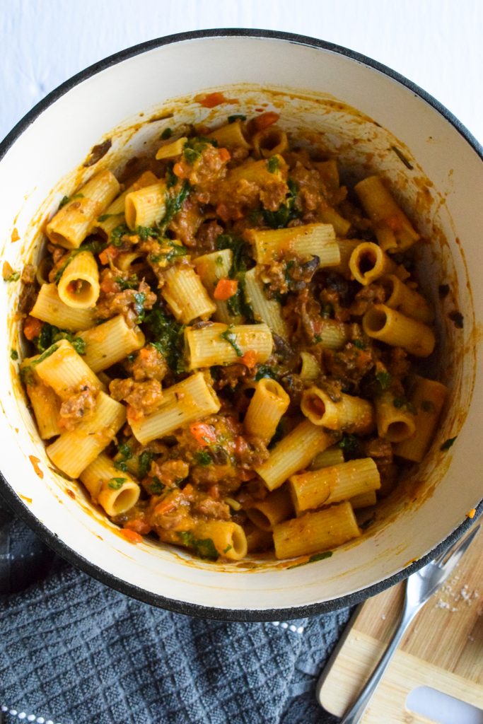 Close up shot of a dutch oven filled with rigatoni with a squash, sausage and mushroom pasta sauce.