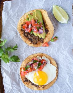 Two black bean breakfast tostadas on a piece of parchment paper atop a baking sheet