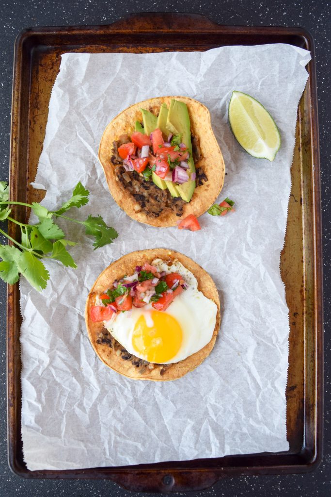 Two black bean breakfast tostadas on a piece of parchment paper atop a baking sheet