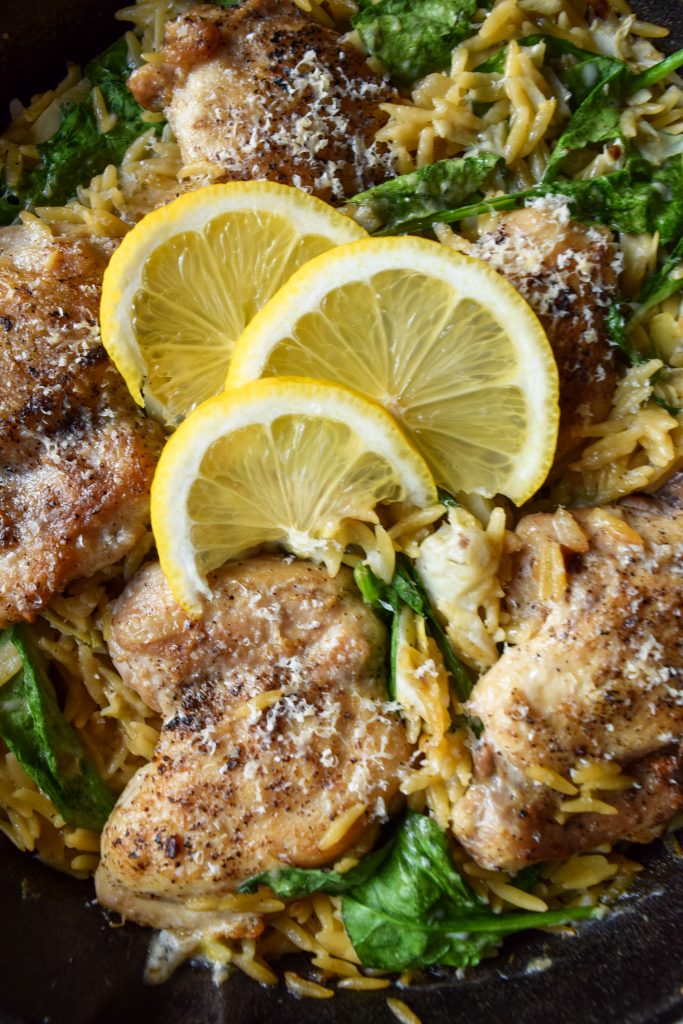 Close up shot of chicken thighs in orzo with spinach, topped with 3 sliced lemons.