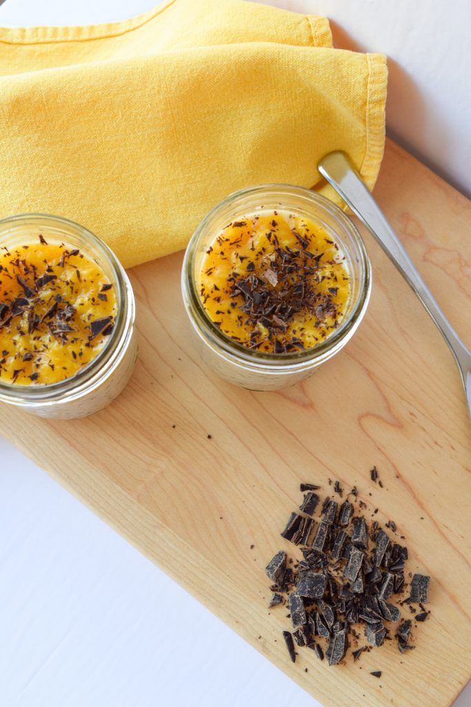 Birds eye view of two mason jars topped with mango coulis and dark chocolate on a wooden cutting board.