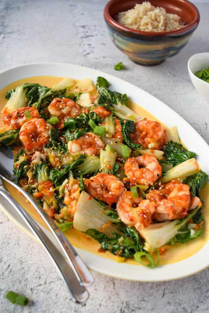 Close up shot of an oblong yellow and white dish filled with garlic shrimp and bokchoy.