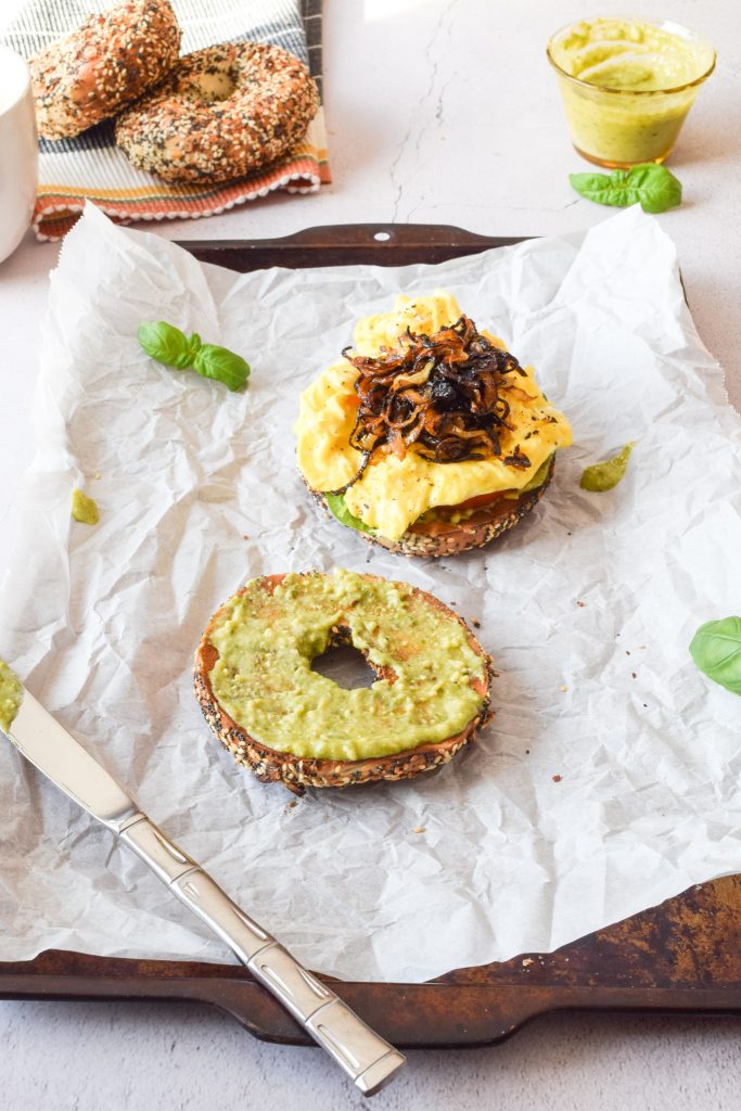 two halves of an everything bagel breakfast sandwich on a baking sheet lined with parchment paper, surrounded by fresh basil