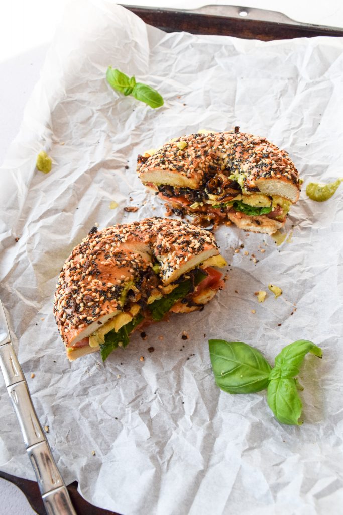 two halves of an everything bagel breakfast sandwich on a baking sheet lined with parchment paper, surrounded by fresh basil