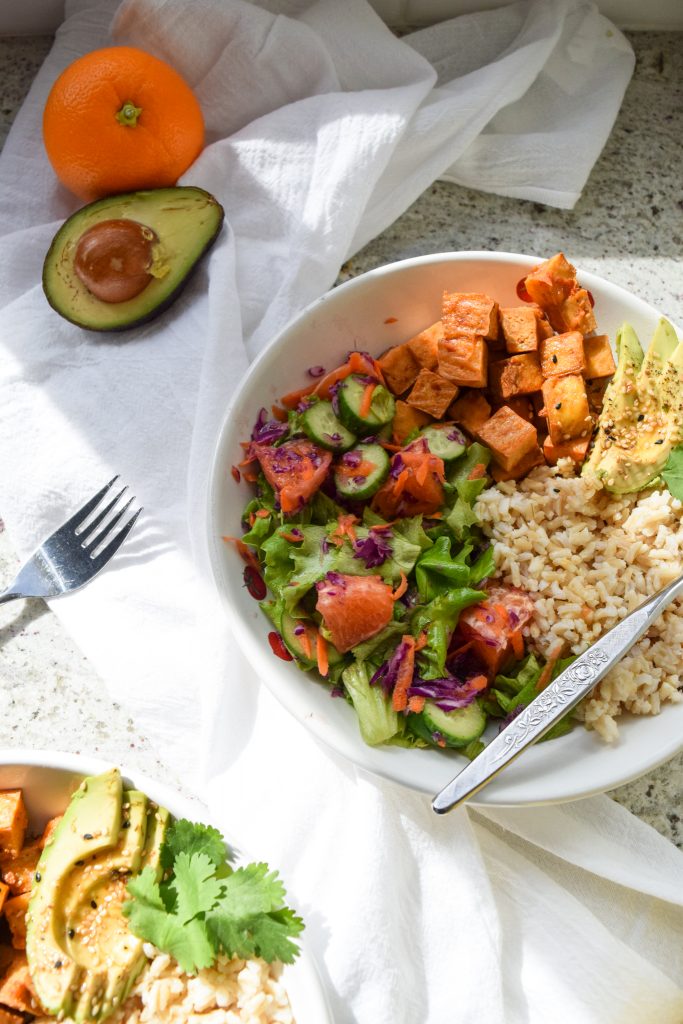 close up shot on a tofu bowl with citrus salad, avocado and brown rice, half an avocado and orange on the side
