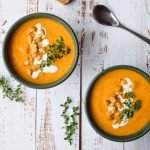 2 green bowls filled with butternut squash soup, topped with cream, squash seeds and fresh thyme.