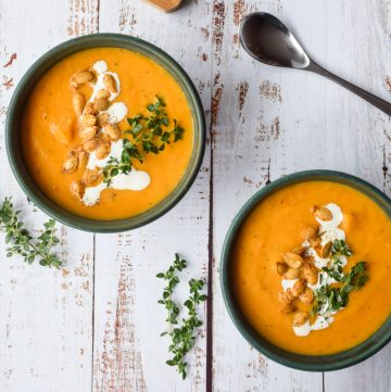 2 green bowls filled with butternut squash soup, topped with cream, squash seeds and fresh thyme.