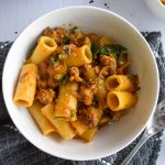 White bowl with squash and sausage pasta on a grey towel