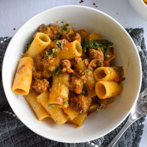 White bowl with squash and sausage pasta on a grey towel