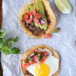 Two black bean breakfast tostadas on a piece of parchment paper atop a baking sheet