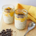 2 small mason jars filled with overnight oats, topped with mango coulis and dark chocolate atop a wooden cutting board.